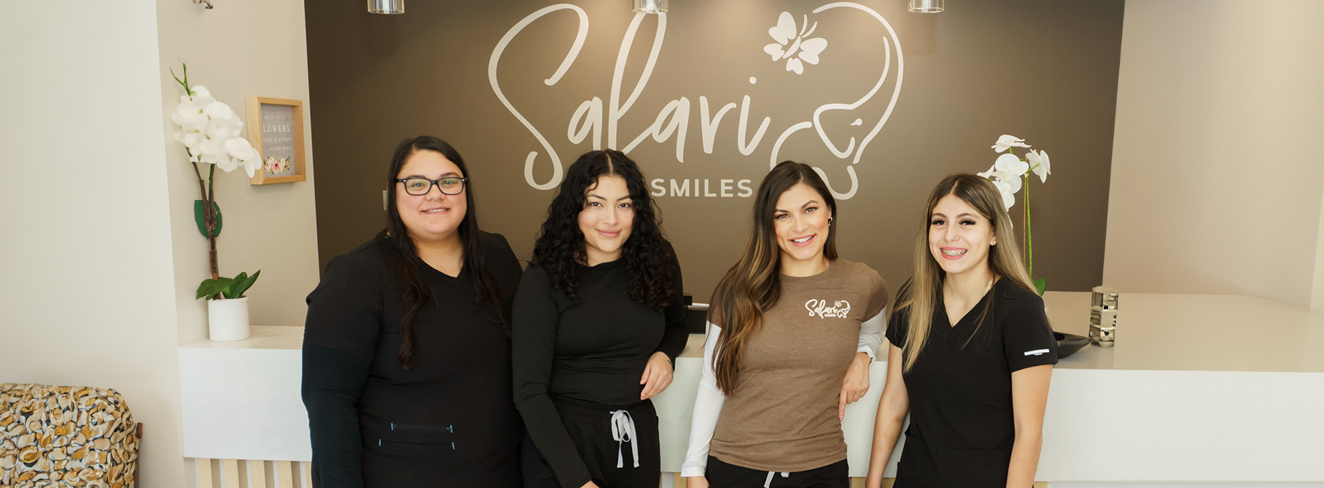 The image shows a group of four individuals posing in front of a storefront with the sign SALVIO visible. They are standing in front of a window display, and there is a potted plant on the left side of the frame.