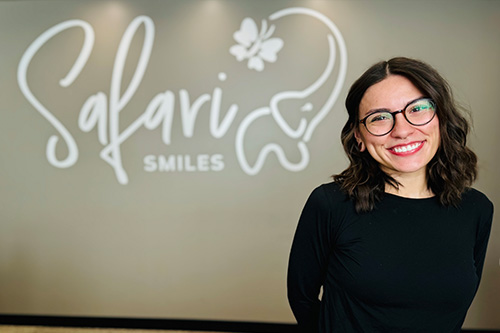 The image features a woman standing in front of a sign that reads Salavri Smiles. She is smiling and wearing glasses.