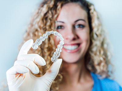 A woman is holding up a transparent dental retainer.