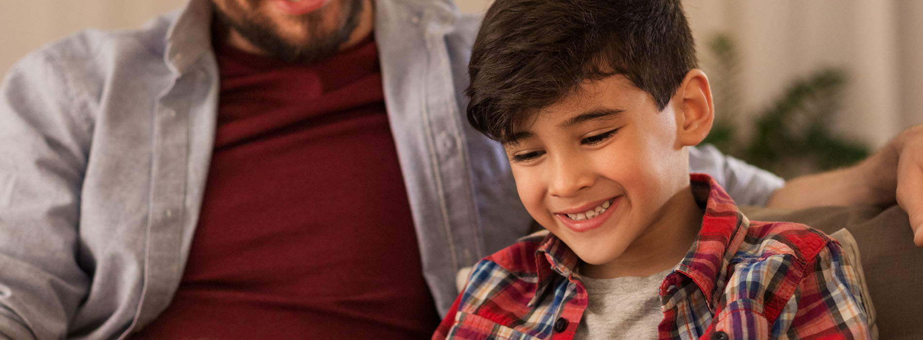A man and a young boy are seated together, smiling at the camera they appear to be in a relaxed indoor setting.